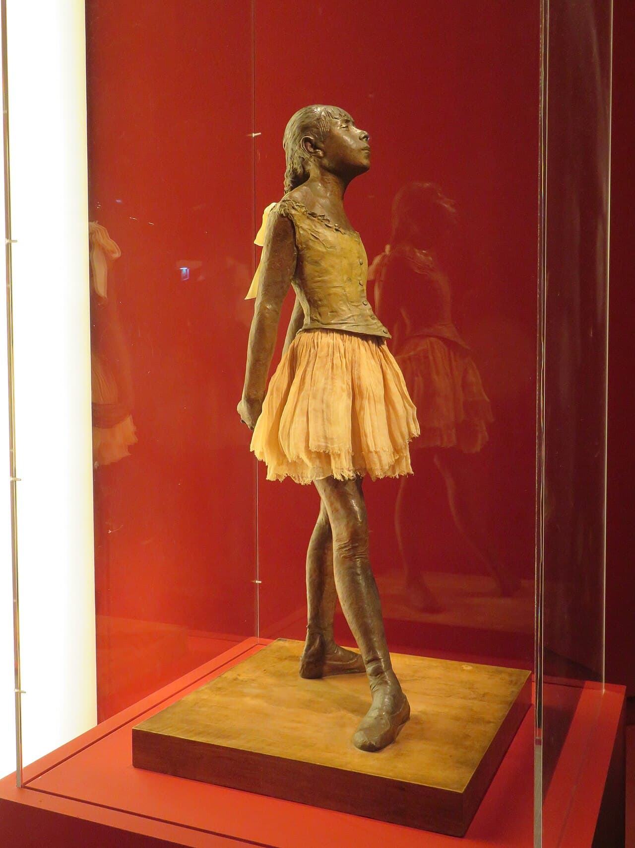 Degas's bronze Little Dancer of Fourteen Years wearing a fabric tutu and satin ribbon, standing in a ballet pose